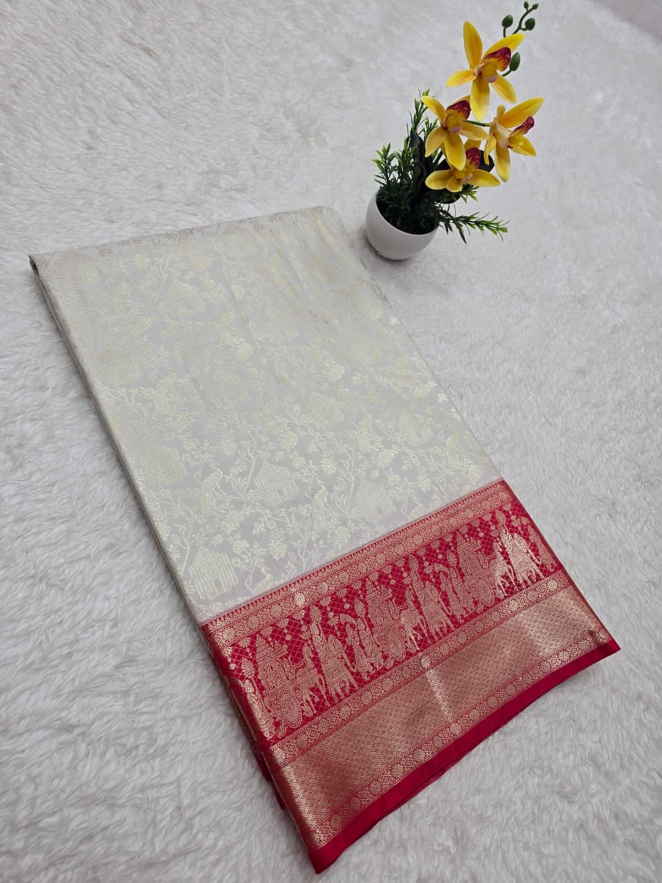 White fabric with a red border on a light gray surface, accompanied by a small potted plant with yellow flowers.