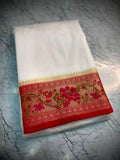 A folded white fabric item, likely a saree or scarf, featuring a decorative border with red, pink, and gold floral embroidery, placed on a gray marble-textured surface.