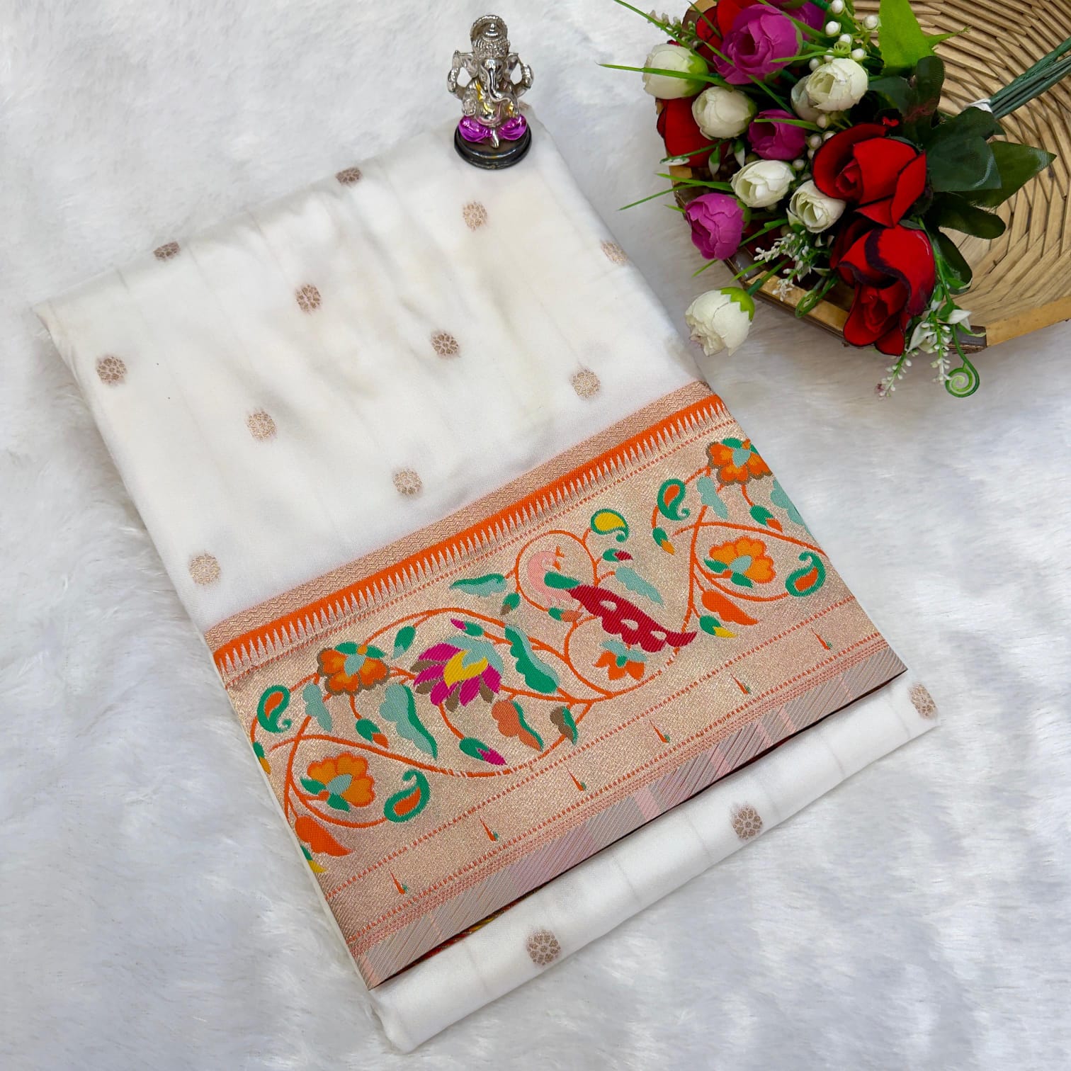 White saree with colorful patterns on a white surface with flowers and jewelry.