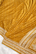 Close-up of a mustard yellow saree with intricate patterns on a white background