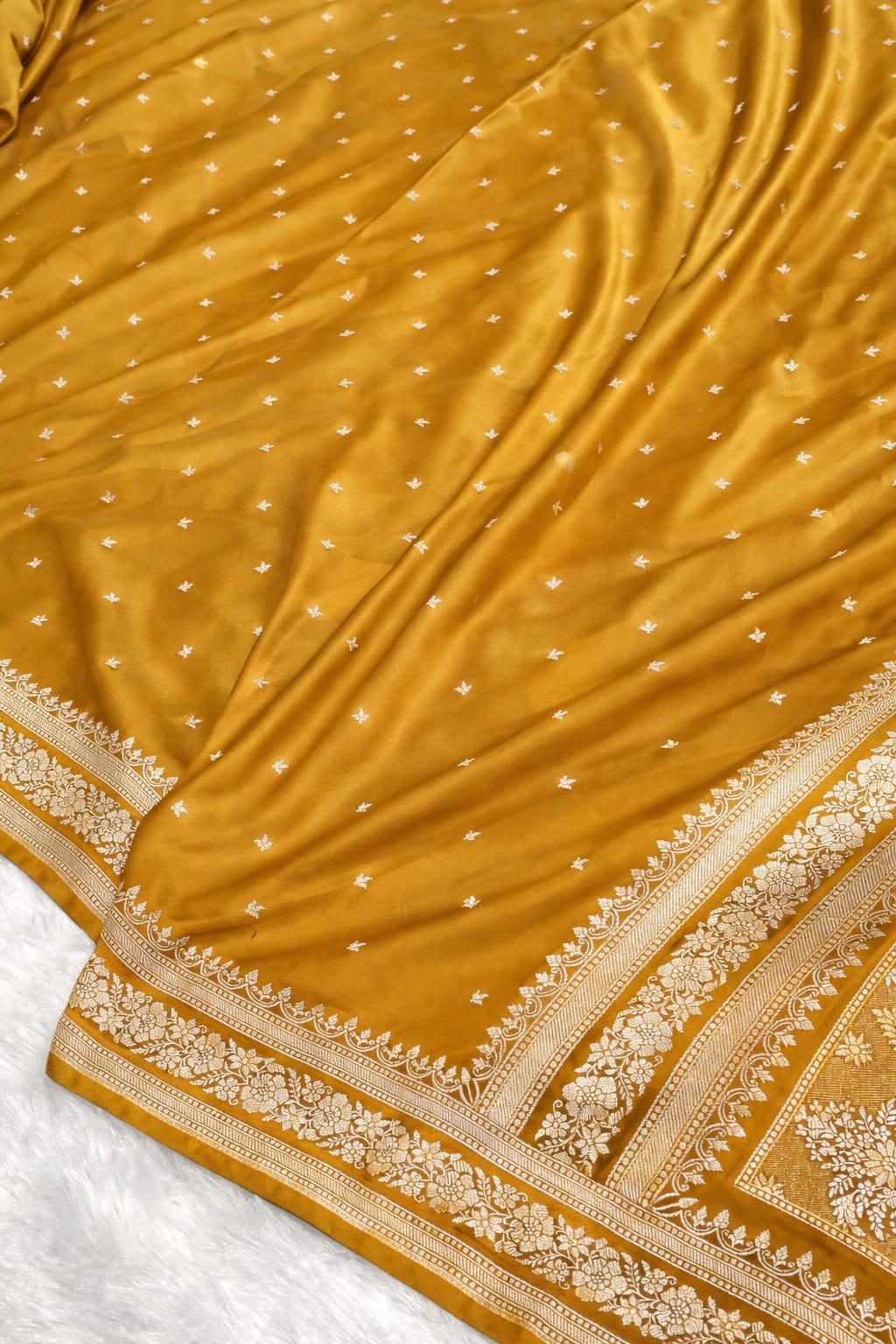 Close-up of a mustard yellow saree with intricate patterns on a white background